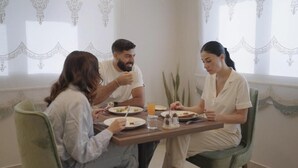 A dining area with a table set for four people, chairs, a window with curtains, and a plant. - Princess Plaza hotel (Ma'an)