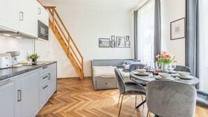 Una cocina moderna con escalera de madera, un comedor con una mesa redonda para dos personas y un ventanal con cortinas.