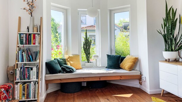 Un coin lecture confortable avec un banc intégré, une bibliothèque et une plante en pot.
