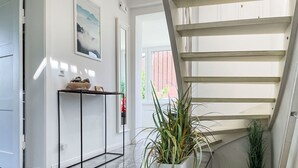 Un intérieur moderne avec un escalier, une console blanche agrémentée d’objets décoratifs et une grande plante en pot.