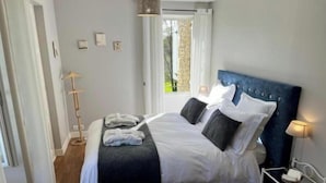 A neatly arranged bedroom with a bed, bedside tables, a floor lamp, and a view of the outdoors. - 
Ancien Haras de la Tour Chambre Le Parc (Lamothe-Landerron)