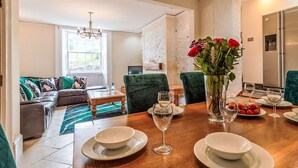 A dining area with a wooden table set for four, surrounded by green upholstered chairs. A vase with red flowers is on the table, and there are plates, glasses, and a bowl. - Wonderful private villa for 9 people with WIFI, TV and pets allowed (Mevagissey)