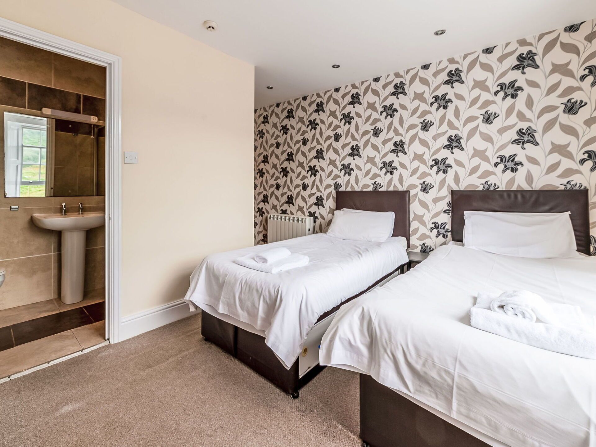 Une chambre d’hôtel avec deux lits, une salle de bain avec un lavabo et un papier peint à motifs.