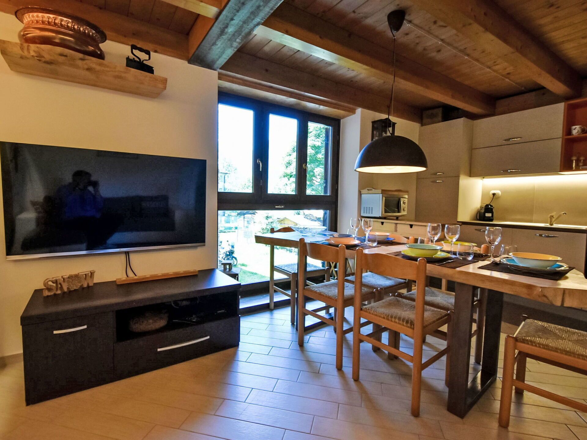 A modern kitchen with a dining area, wooden furniture, and a large flat-screen TV.