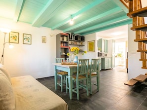 Een eetgedeelte met een tafel en stoelen, een boekenkast, en een keuken op de achtergrond.