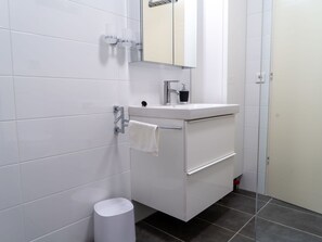 A modern bathroom with white tiles, a white sink, a mirror, and a towel rack. - Beautiful apartment for 3 people with A/C, WIFI, TV and balcony (Strobl)