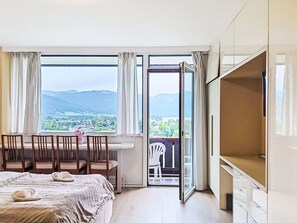 A hotel room with a bed, a dining table with chairs, a TV, and a balcony with a view of mountains. - Nice apartment for 3 guests with WIFI, A/C, TV and balcony (Strobl)