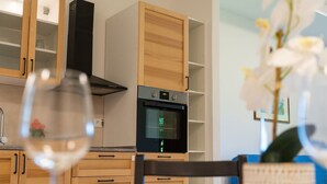 A modern kitchen with wooden cabinets, a built-in oven, and a dining area with a table and chairs.