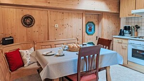 A cozy wooden dining area with a table set for two, a bench with cushions, and a kitchen with a stove and coffee maker. - Lovely apartment for 4 people (Hippach)
