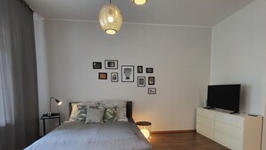 A modern bedroom with a bed, bedside tables, a TV, and framed pictures on the wall. - Nice apartment for 2 guests with TV and balcony (Magdeburg)