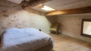 Una camera da letto con un letto grande, pavimento in legno, una sedia in vimini e un lucernario.
