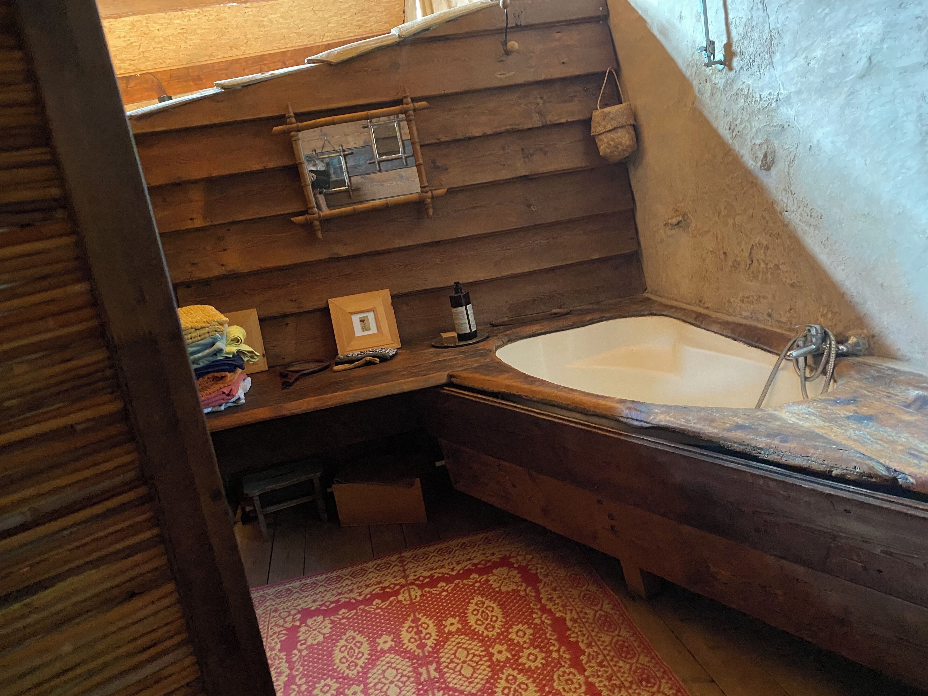 Une salle de bain rustique en bois, dotée d’une grande baignoire, d’étagères en bois et d’un petit meuble en bois.