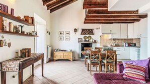 Una sala de estar acogedora con techo de madera, un comedor con mesa y sillas, y una cocina con armarios blancos y salpicadero de azulejos.