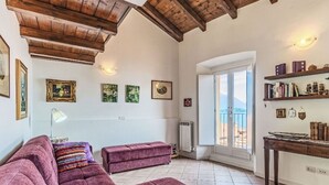 Una sala de estar con techo de madera, un sofá, una mesa con libros y vistas a través de un ventanal.