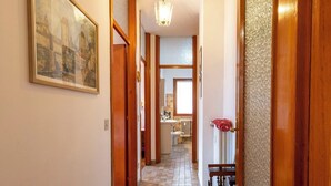 A hallway with a tiled floor, wooden doors, a hanging light fixture, and a painting on the wall.