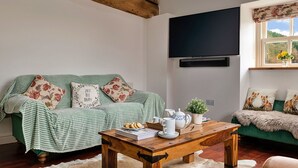 A cozy living room with a green sofa, wooden coffee table, and a flat-screen TV mounted on the wall.