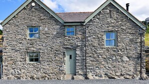 A stone building with a gabled roof, a central door, and two windows on the upper floor.