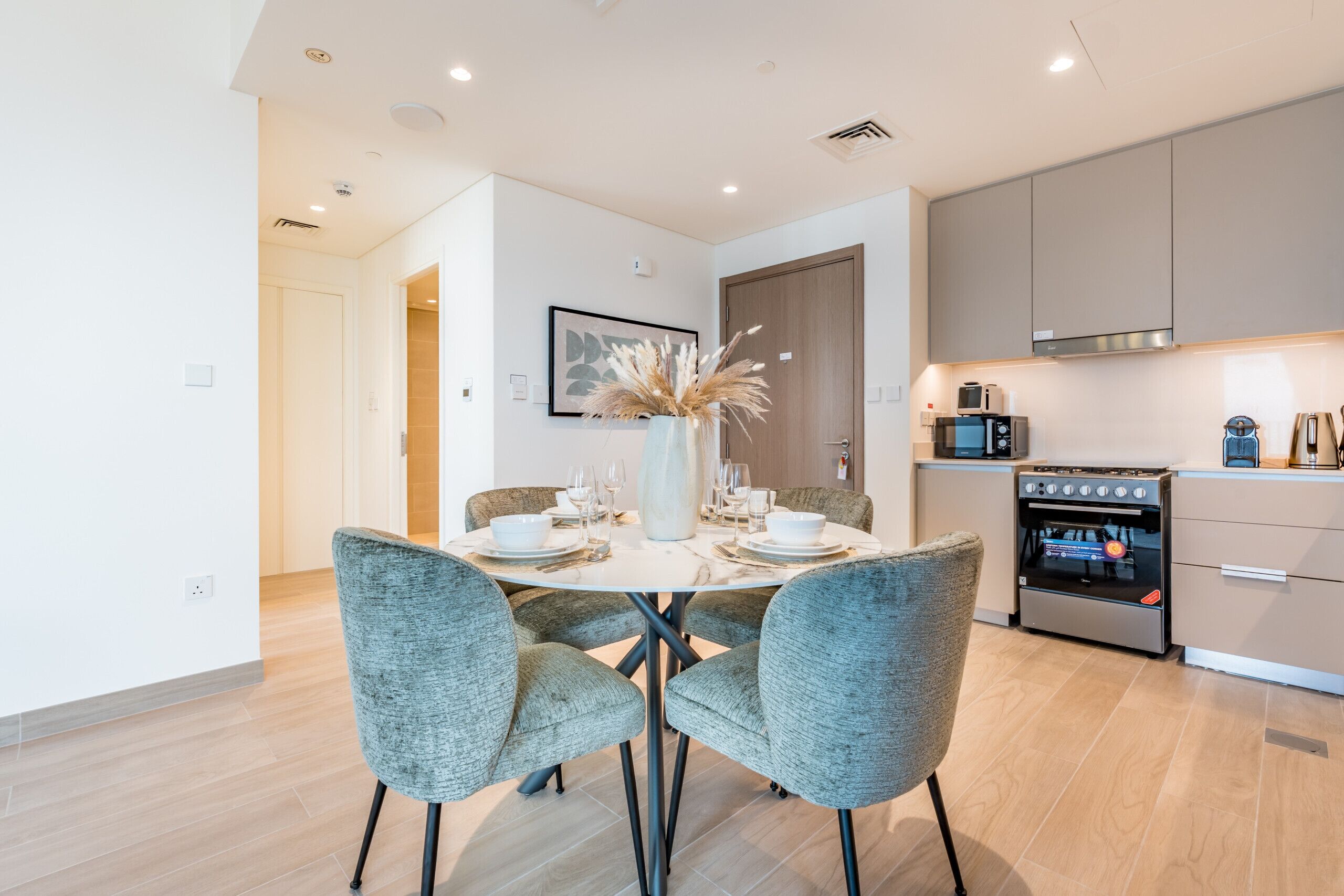 A modern kitchen with a built-in oven and microwave, a dining table set with plates and glasses, and a vase with dried plants.