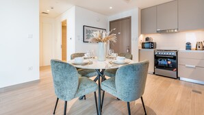 A modern kitchen with a built-in oven and microwave, a dining table set with plates and glasses, and a vase with dried plants. - Creek Views 1BR, Short Drive to Ras Al Khor Sanctuary and Festival City Mall (Dubai)