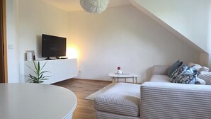 Una sala de estar moderna con un sofá blanco, un sillón gris, una mesita blanca y un televisor sobre un mueble blanco.