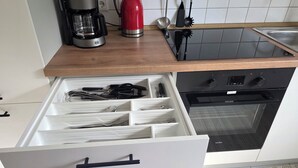 Una cocina con un organizador de cajones, una cafetera y un hervidor rojo sobre la encimera.