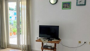 A living room with a television on a wooden stand, a wall clock, and a picture frame. - Apartment A2 dvije spavaće sobe, Garden Terrace 40 m2 with Outdoor Shower (Ražanj)