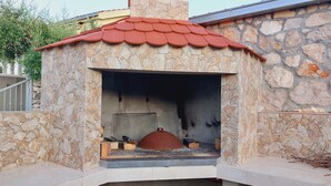 A stone-built outdoor fireplace with a red tiled roof, a metal grate, and a chimney. - Apartment A2 dvije spavaće sobe, Garden Terrace 40 m2 with Outdoor Shower (Ražanj)