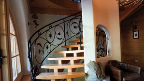 A wooden spiral staircase with a wrought iron railing, a stone wall, and a leather chair in a rustic interior.