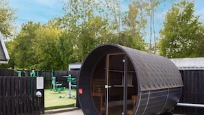 En cylindrisk, modern byggnad med ett böjt tak, eventuellt ett podhotell eller ett unikt boende, placerad i ett välordnat område med ett staket av trä och grönska i bakgrunden.