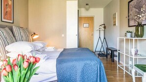 A bedroom with a bed, pillows, a bedside lamp, a desk, a chair, a shelf with decorative items, and a door leading to another room. - 2 Person Holiday Park Home in Bastad (Bastad)