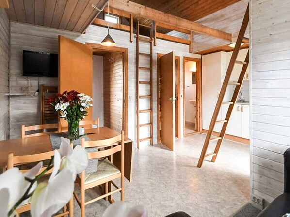 Un interior de madera con comedor, un televisor montado en la pared y una escalera que sube a otro nivel.