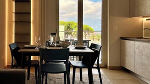A dining area with a table set for four, a kitchen adjacent to the dining space, and a view of greenery and a body of water through large windows.