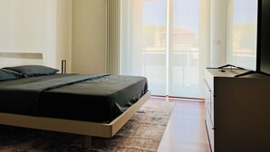 A modern bedroom with a bed, a television, and a sliding glass door leading to a balcony.