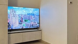 A living room with a flat-screen TV mounted on a cabinet, a grey sofa, and a tiled floor.