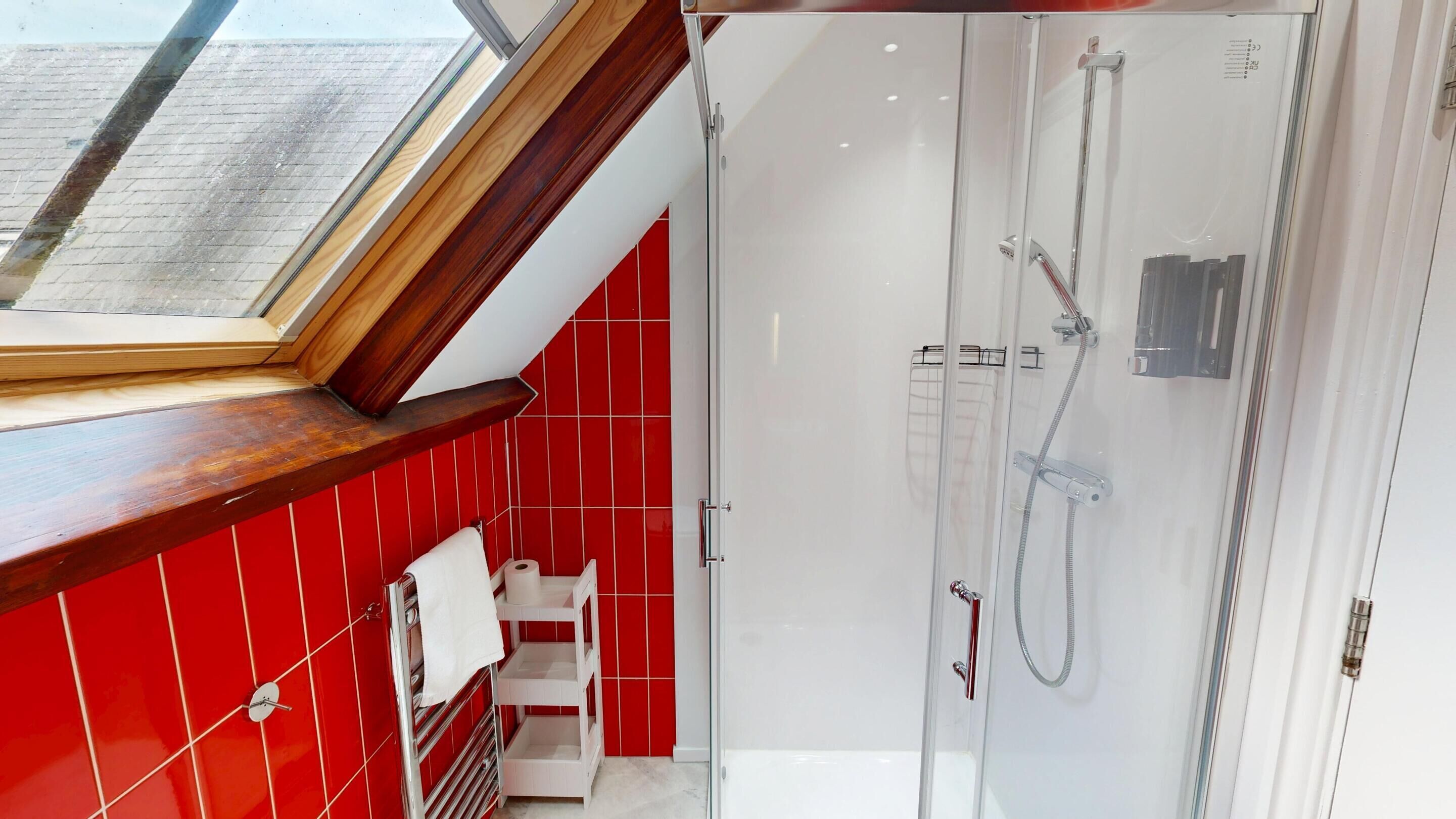 A modern bathroom with a skylight, red tiled walls, a glass shower enclosure, and a white sink.
