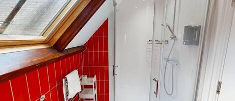 A modern bathroom with a skylight, red tiled walls, a glass shower enclosure, and a white sink.