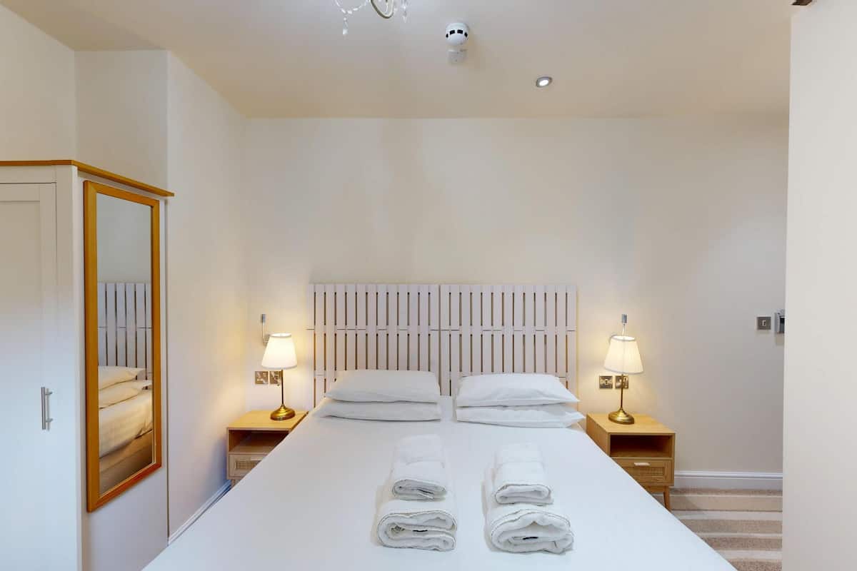 A hotel room with a large bed, two bedside lamps, a wooden headboard, a mirror, and a wardrobe.