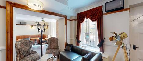 A room with a sofa, two patterned armchairs, a small table, and a lamp.