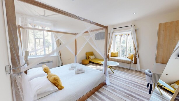 A bedroom with a four-poster bed, a bedside table, a small sofa, and a mirror. - High Tor Hotel (Matlock)