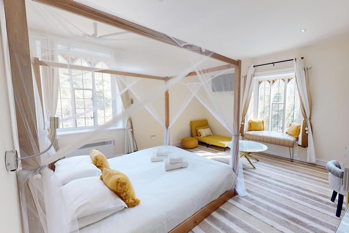 A bedroom with a four-poster bed, a bedside table, a small sofa, and a mirror.