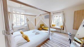 Quarto com cama de dossel, mesa de cabeceira, um pequeno sofá e um espelho.