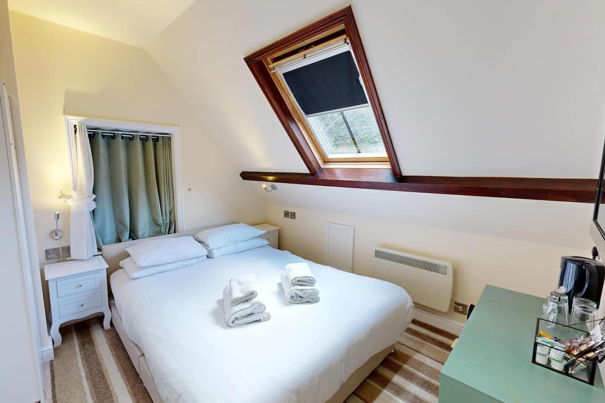 A hotel room with a bed, bedside table, and a window with a view of greenery.
