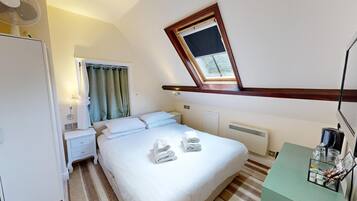 A hotel room with a bed, bedside table, and a window with a view of greenery.
