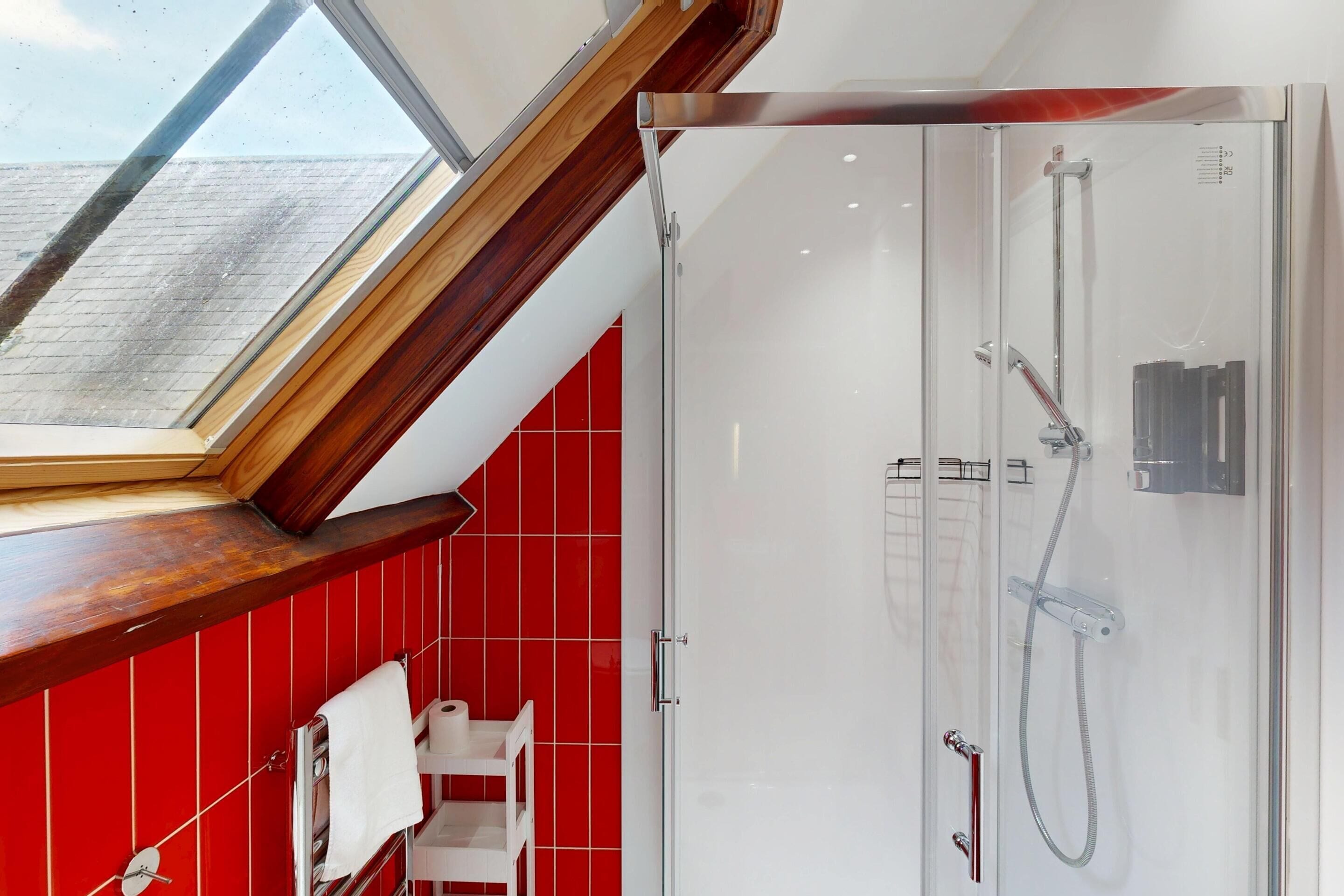 A modern bathroom with a skylight, a glass-enclosed shower, and red tiled walls.