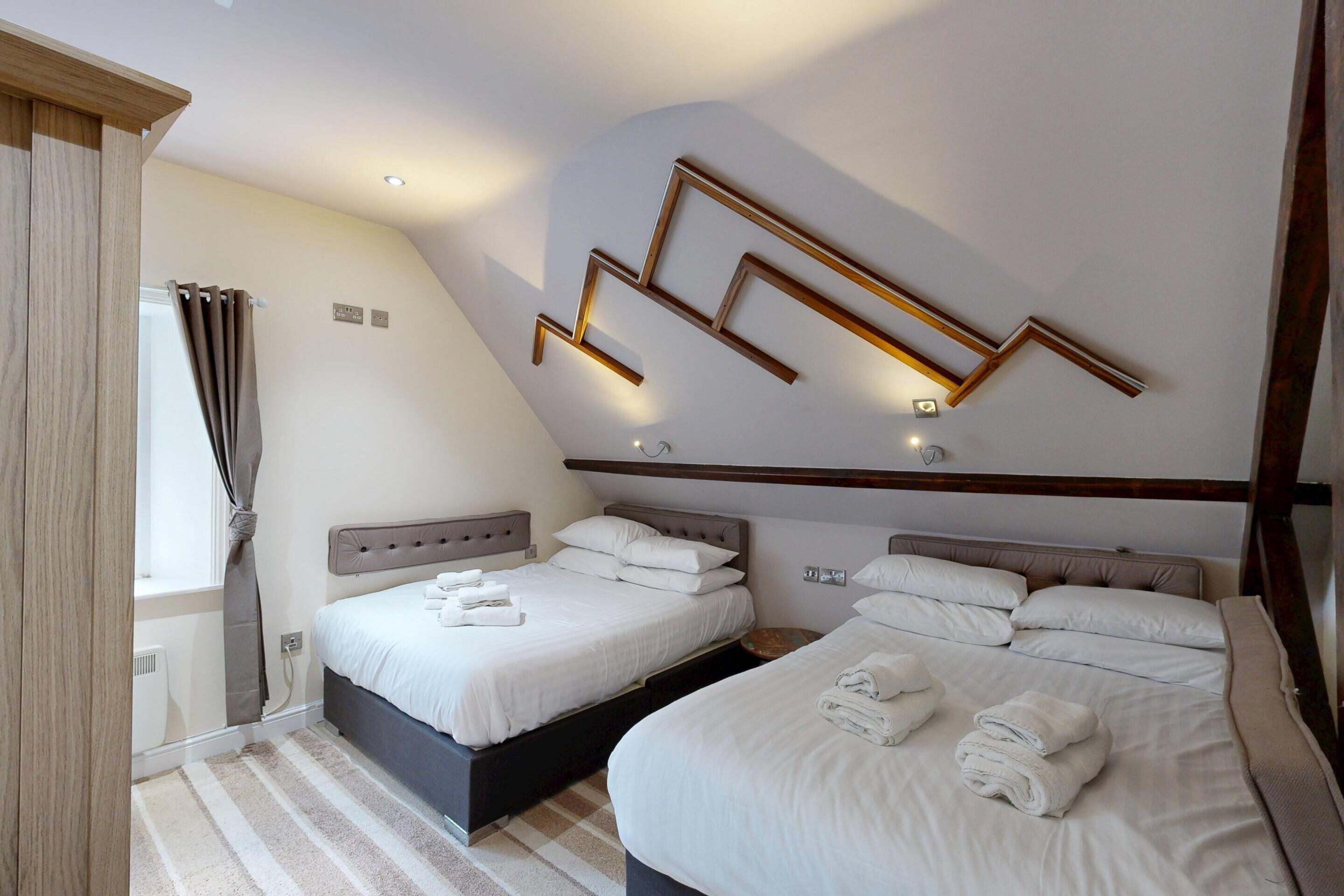 Una habitación de hotel moderna con dos camas, techo de madera y lámpara con diseño geométrico.