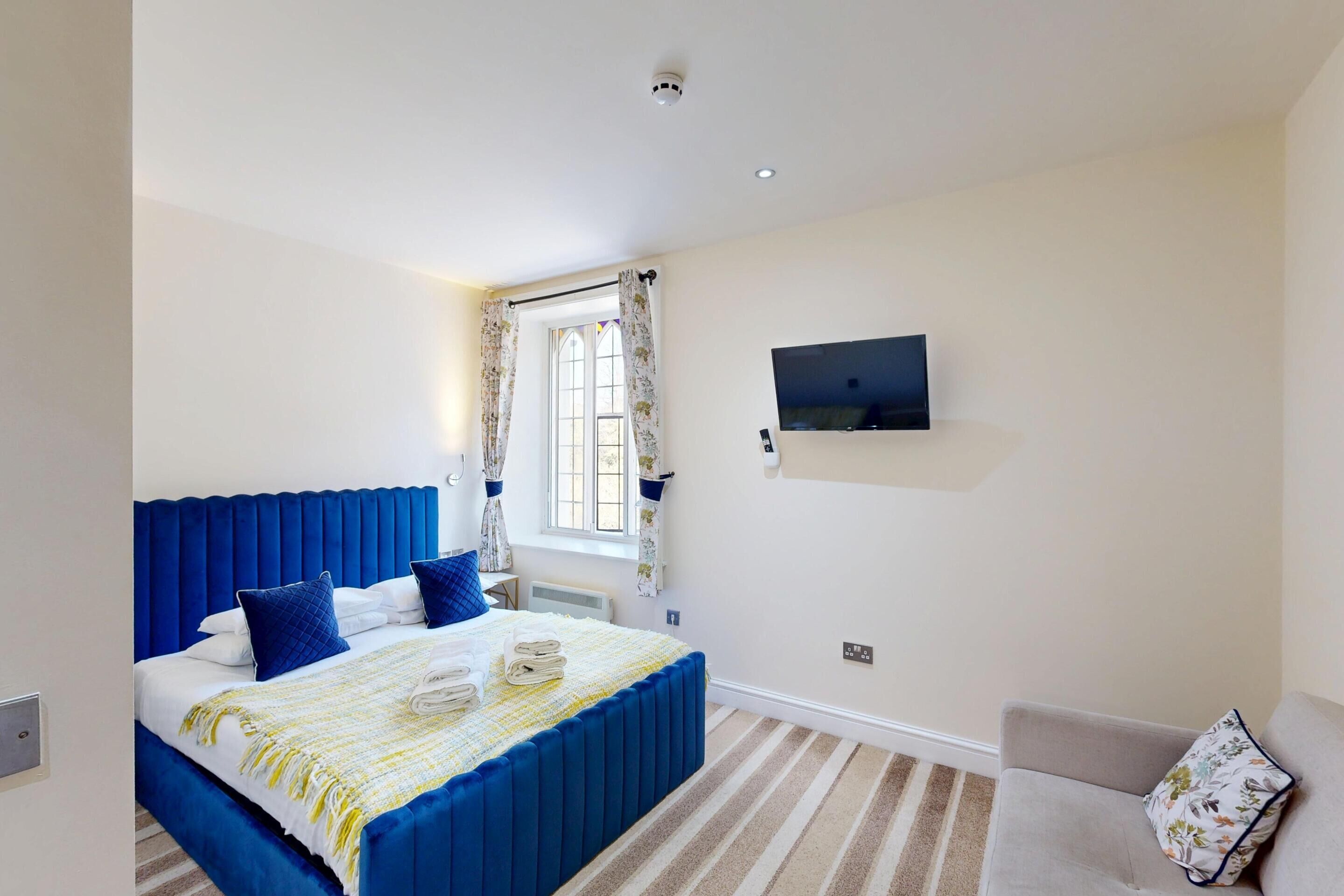 A bedroom with a large bed, a television mounted on the wall, and a window with curtains.