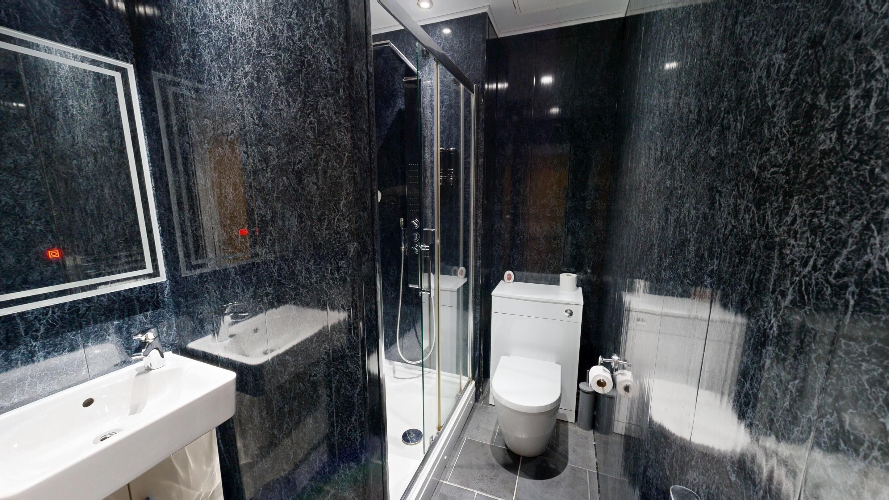 A modern bathroom with a glass-enclosed shower, a white toilet, and a sink with a mirror.