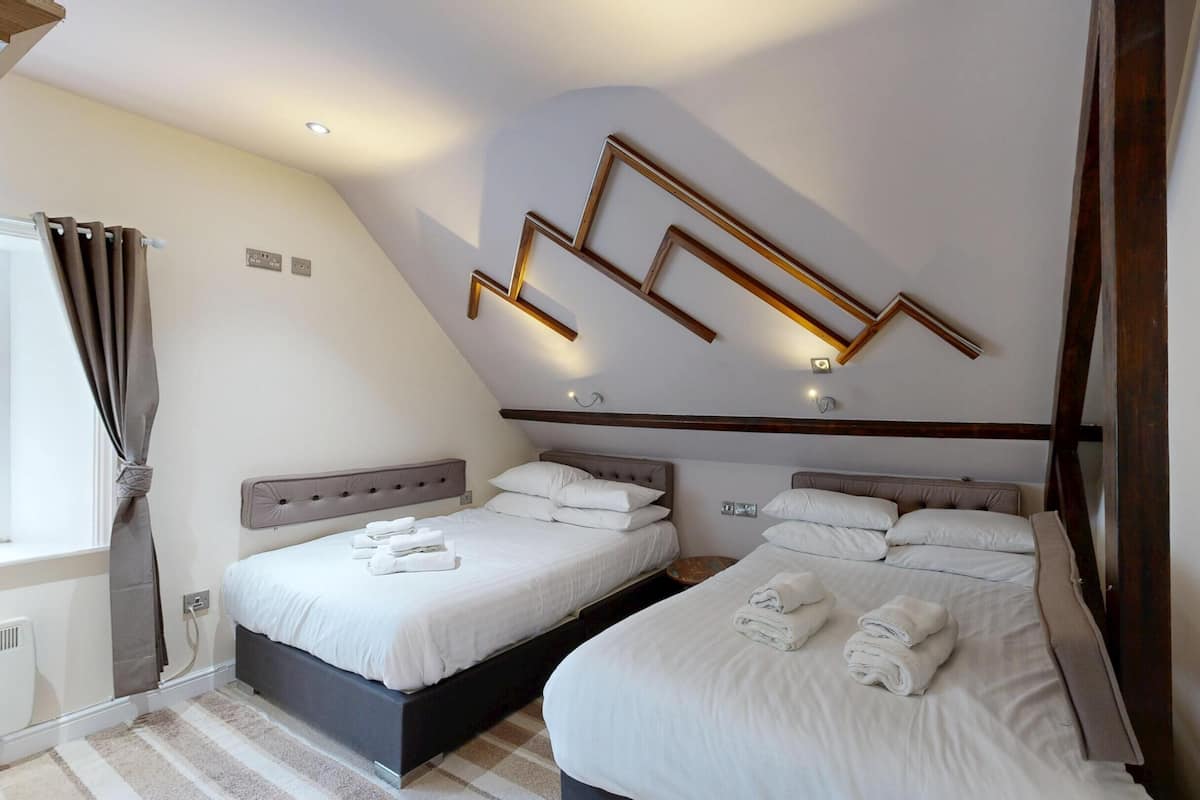 A bedroom with two beds, a modern light fixture, and a window with curtains.