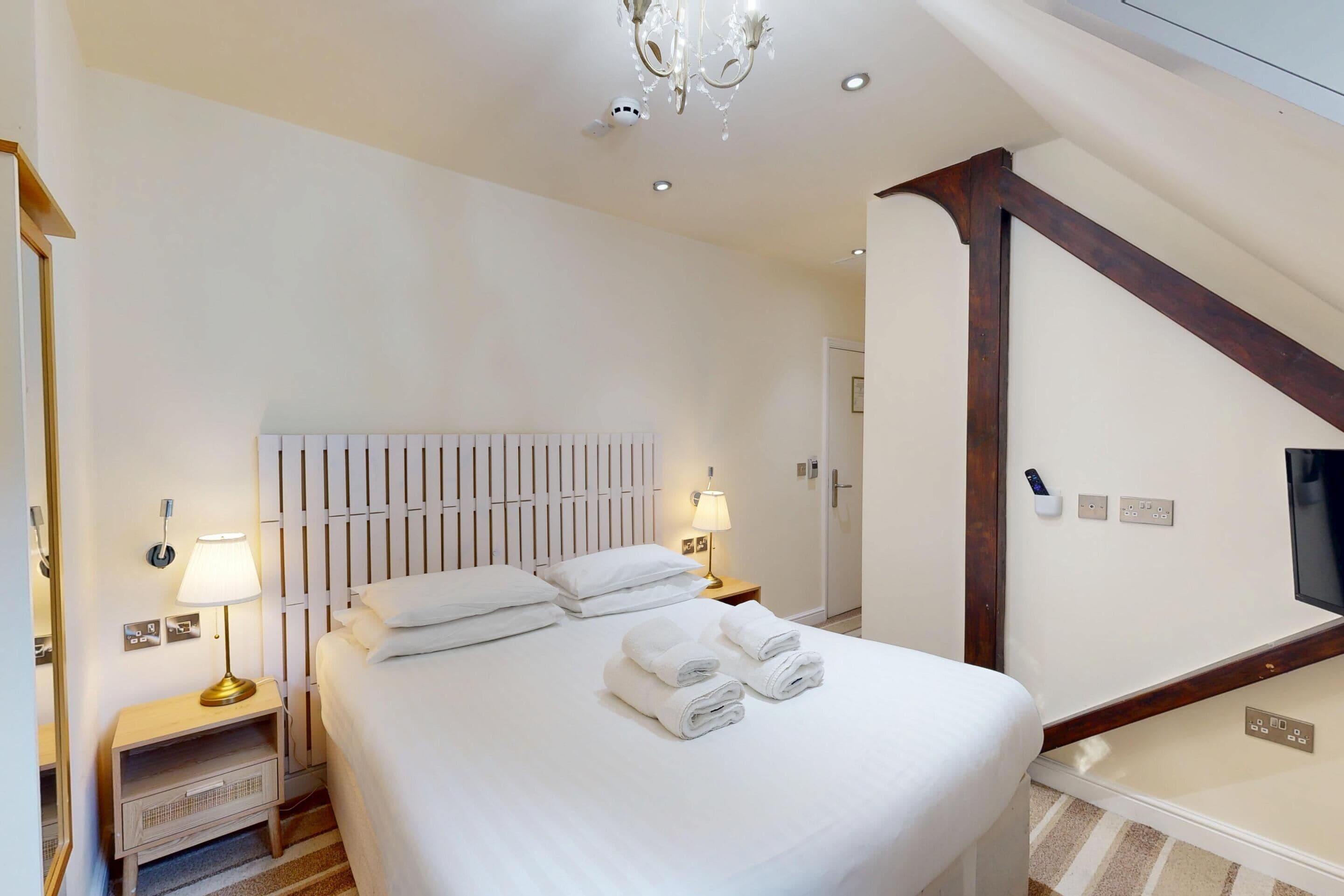 A hotel room with a large bed, two bedside lamps, a white headboard, and a chandelier.