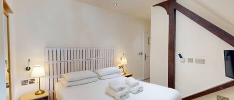 A hotel room with a large bed, two bedside lamps, a white headboard, and a chandelier.